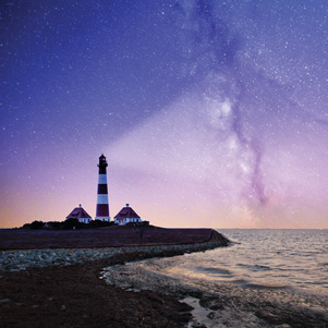 Unter dem Sternenhimmel mit einem Leuchtturm